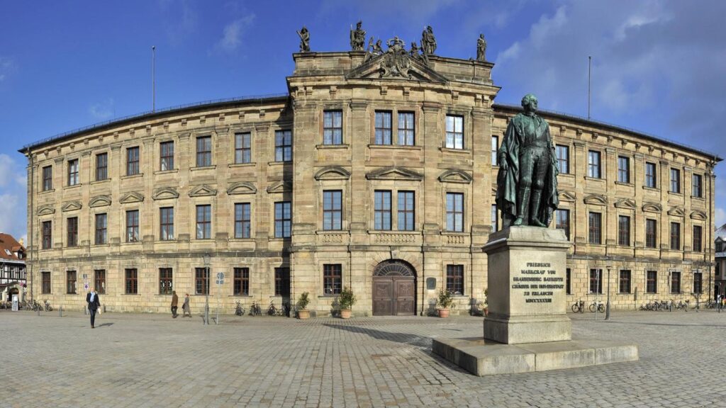Grand facade of FAU Erlangen-Nuremberg with a prominent statue in the foreground, highlighting the university's architectural heritage.