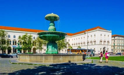 Historic building of the Ludwig Maximilian University of Munich (LMU Munich) with a fountain in the foreground and students walking nearby.
