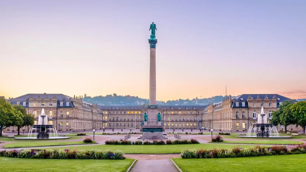 Majestic view of Stuttgart's historic palace square featuring a tall column, fountains, and lush gardens during sunset, symbolizing the city’s cultural and academic significance.